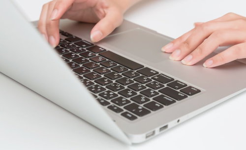 銀色のノートパソコンでタイピングする両手