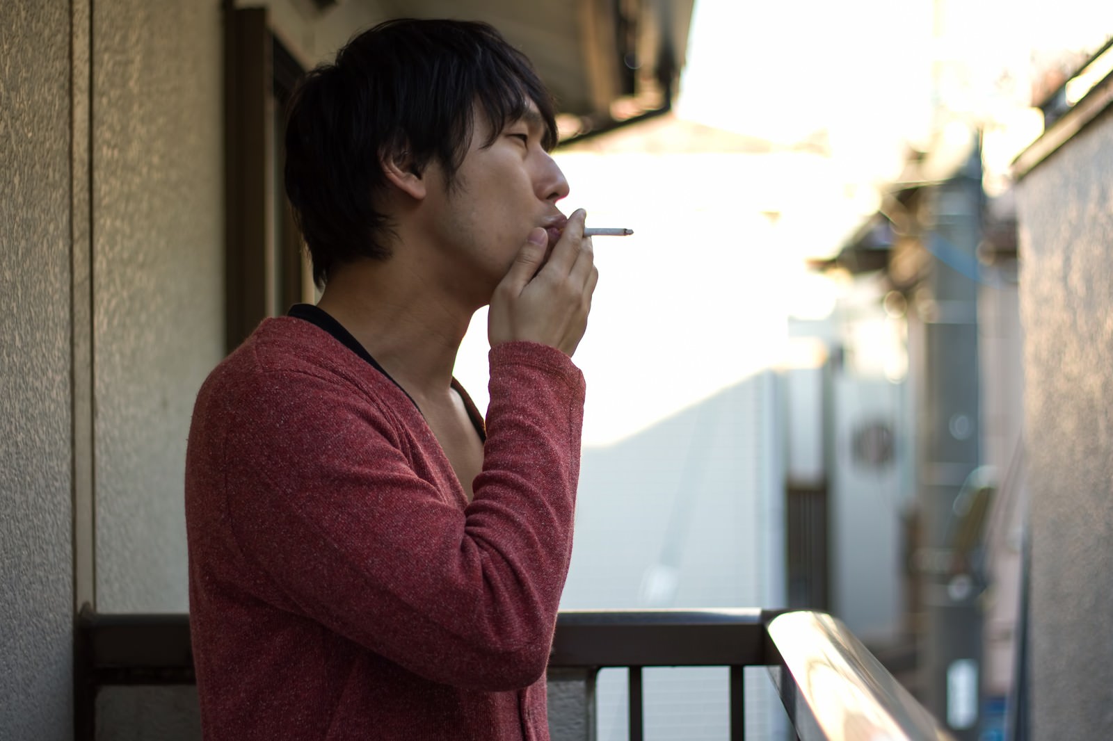 ベランダで口元に手を当てる赤い服の人物［モデル：大川竜弥］