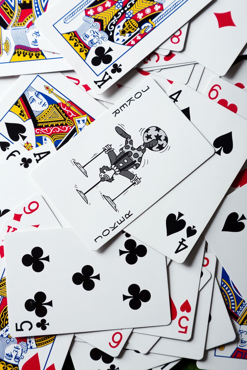 白い背景に散らばったトランプとジョーカー。赤と黒のスーツが見える