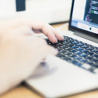 ノートパソコンでコーディング作業をするエンジニアの腕と手元の写真