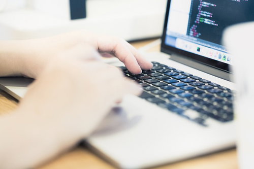 ノートパソコンでコーディング作業をするエンジニアの腕と手元