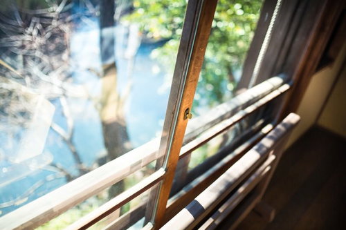 窓辺に立てかけた複数の絵筆と外の緑の木々が見える室内