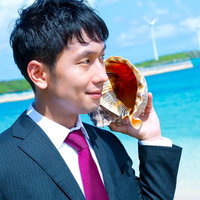 海岸で大きな貝殻を耳に当てるスーツ姿のビジネスマンの写真