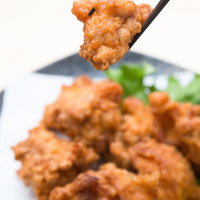 箸でつまんだ唐揚げとレモンや緑の野菜が盛られた皿の写真