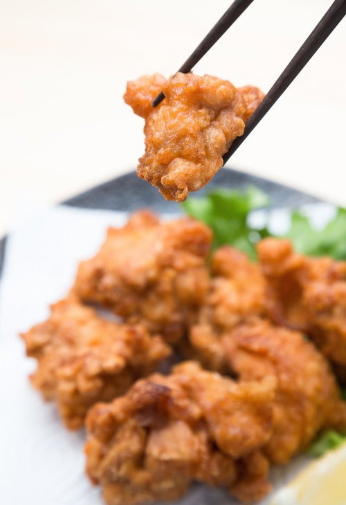 箸でつまんだ唐揚げとレモンや緑の野菜が盛られた皿