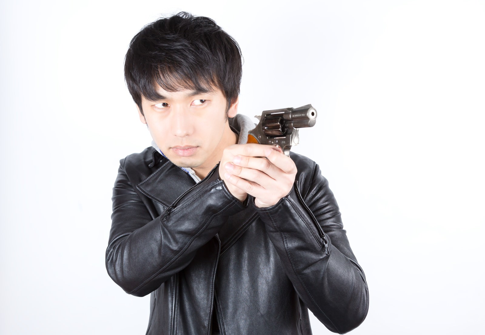 黒い革ジャケットの男性が白い背景の前で両手で拳銃を構えている［モデル：大川竜弥］
