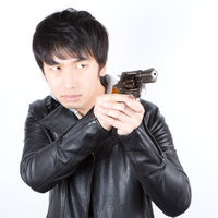 両手で拳銃を構える革ジャケットの男性の写真