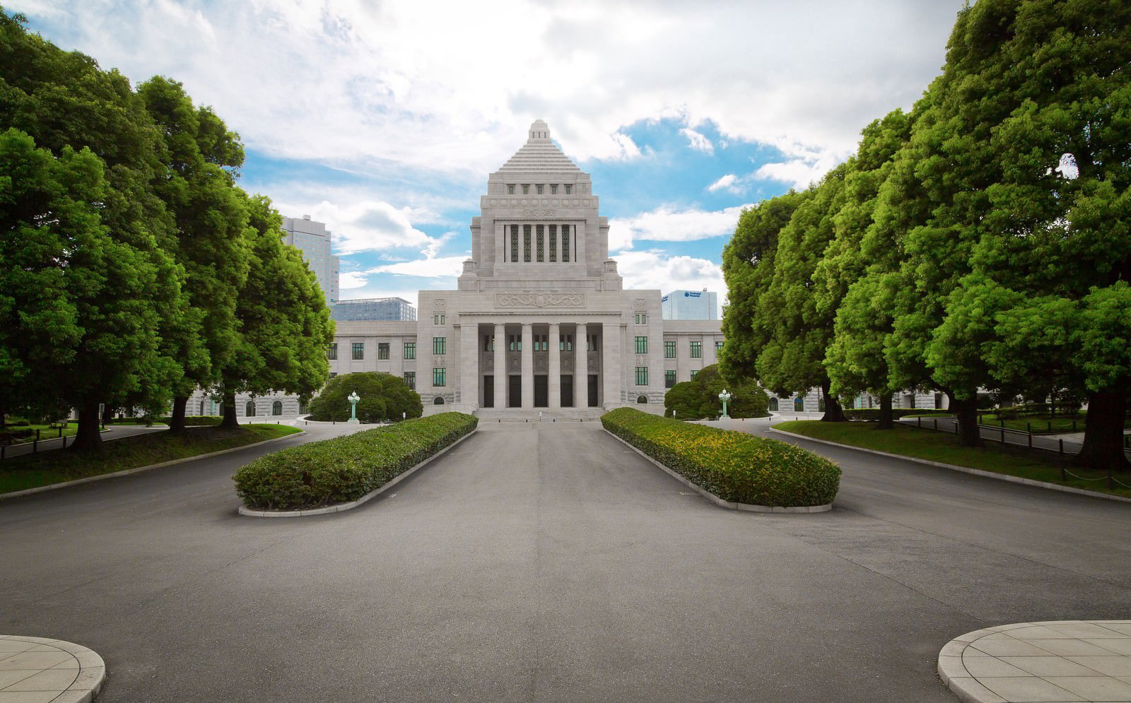 中央にドーム屋根を持つ白い石造りの国会議事堂を、緑の並木越しに見た正面景観