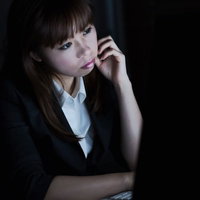 暗いオフィスでパソコンの前に座り顔に手を当てる女性の写真