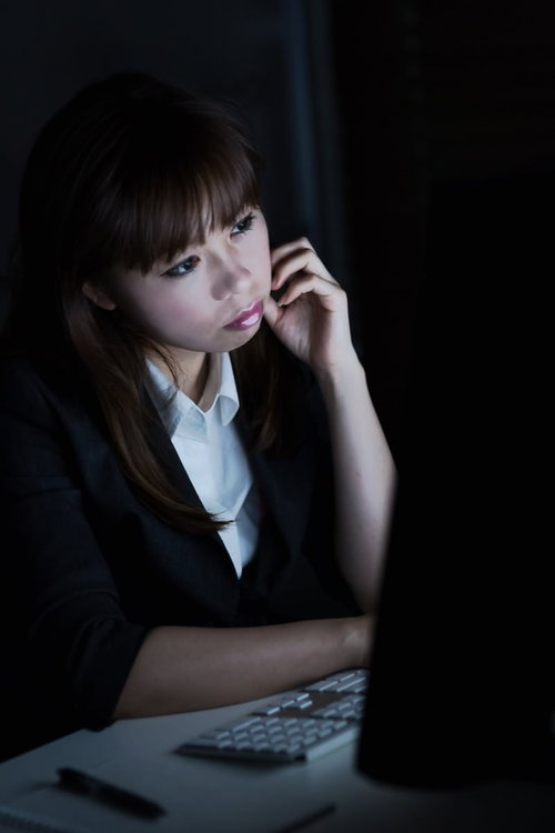 暗いオフィスでパソコンの前に座り顔に手を当てる女性