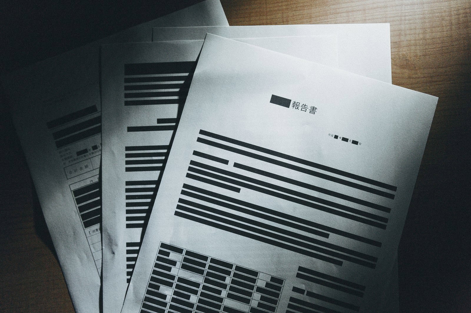 白い報告書が木製机に積み重ねられ、黒いマーカーで塗りつぶされた複数行と棒グラフが見える