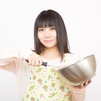 ボウルと泡立て器を持つエプロン姿の笑顔の女性の写真