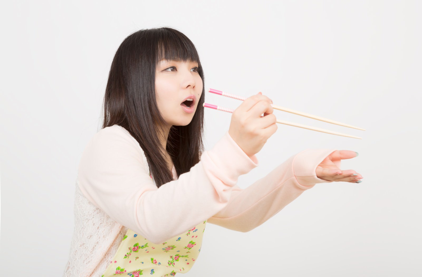 箸を口元に近づけて味見させるエプロン姿の女性［モデル：Lala］
