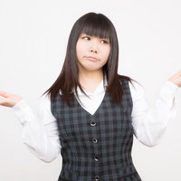 両手を広げて困惑するチェック柄ベストの女性の写真