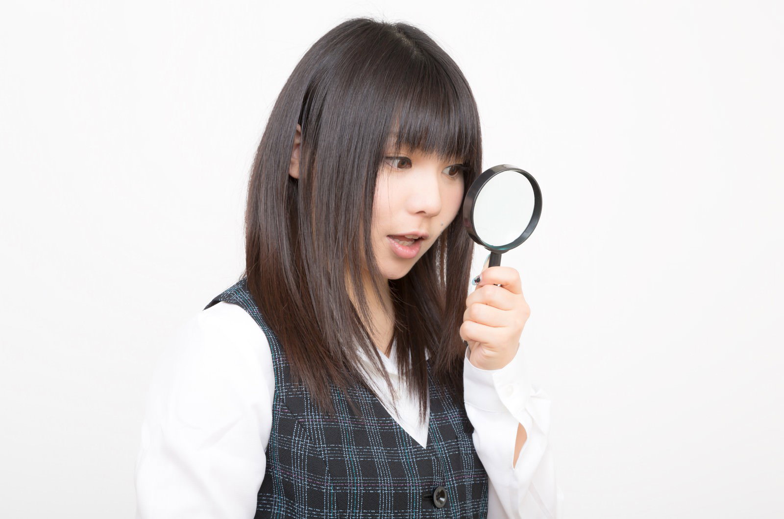 チェック柄ベストの女性が虫眼鏡を顔の横に掲げている［モデル：Lala］