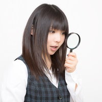 虫眼鏡を顔の横に掲げるチェック柄ベストの女性の写真
