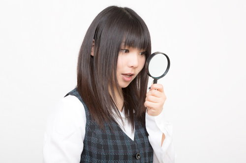 虫眼鏡を顔の横に掲げるチェック柄ベストの女性