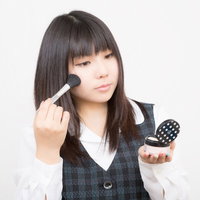化粧ブラシとパウダーケースを持つチェック柄ベストのOLの写真