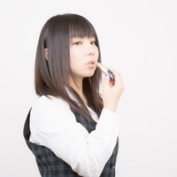 口紅を塗るチェック柄ベストの女性の写真