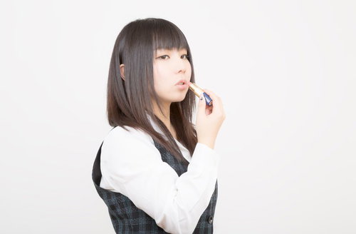 口紅を塗るチェック柄ベストの女性