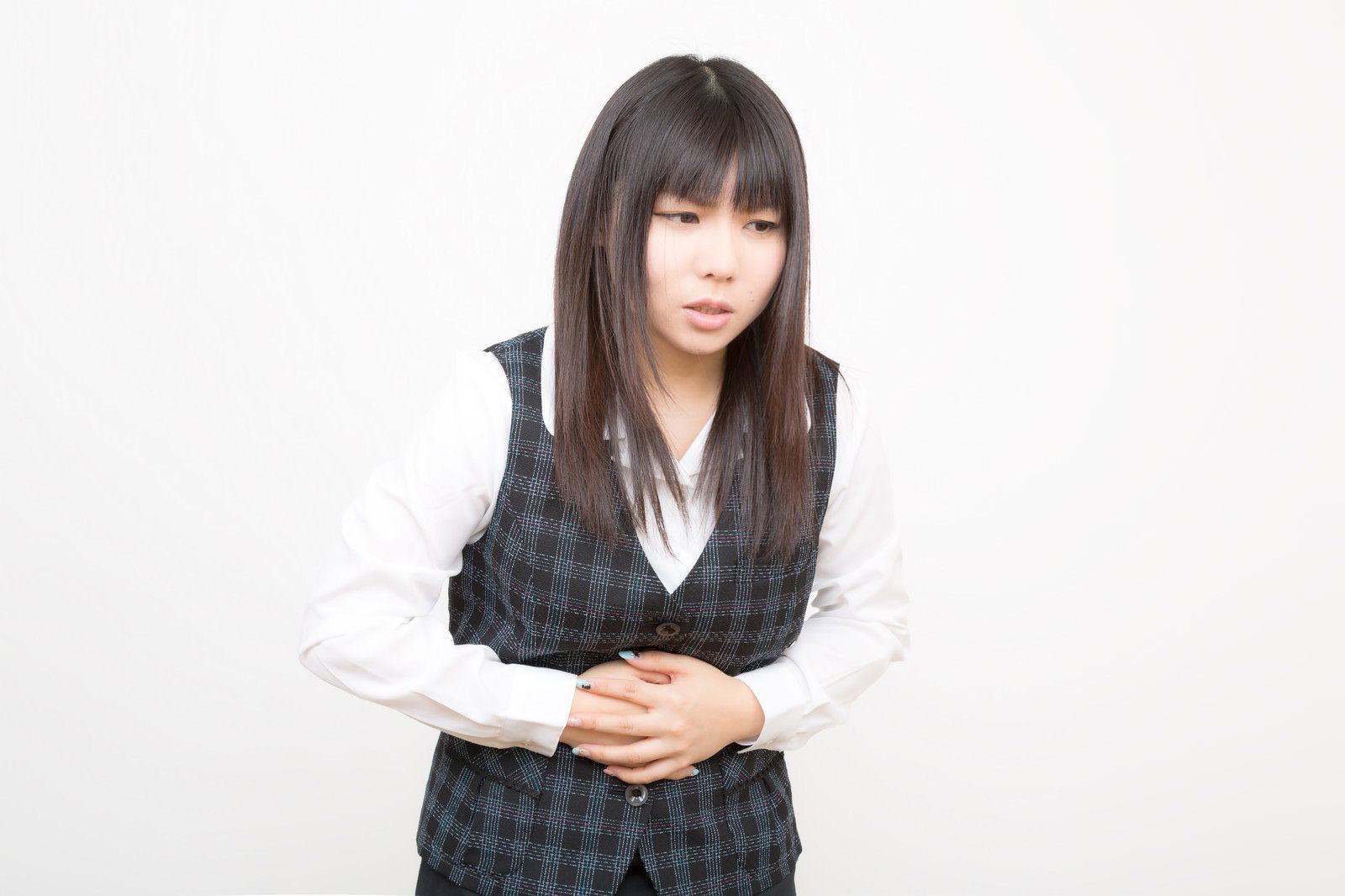 チェック柄ベストの女性が両手をお腹の前で組んで押さえている［モデル：Lala］