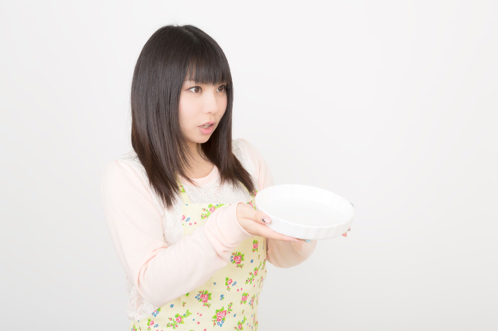花柄エプロンの女性が白い皿を両手で前に差し出している［モデル：Lala］