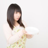 白い皿を両手で差し出すエプロン姿の女性の写真