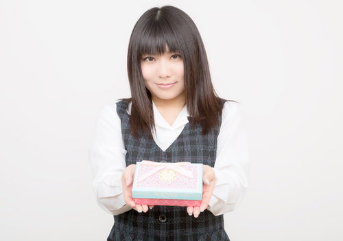 ピンクと水色の箱を両手で持つチェック柄ベストのOL