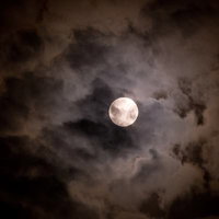 厚い雲の間から見える夜空に浮かぶ満月の写真