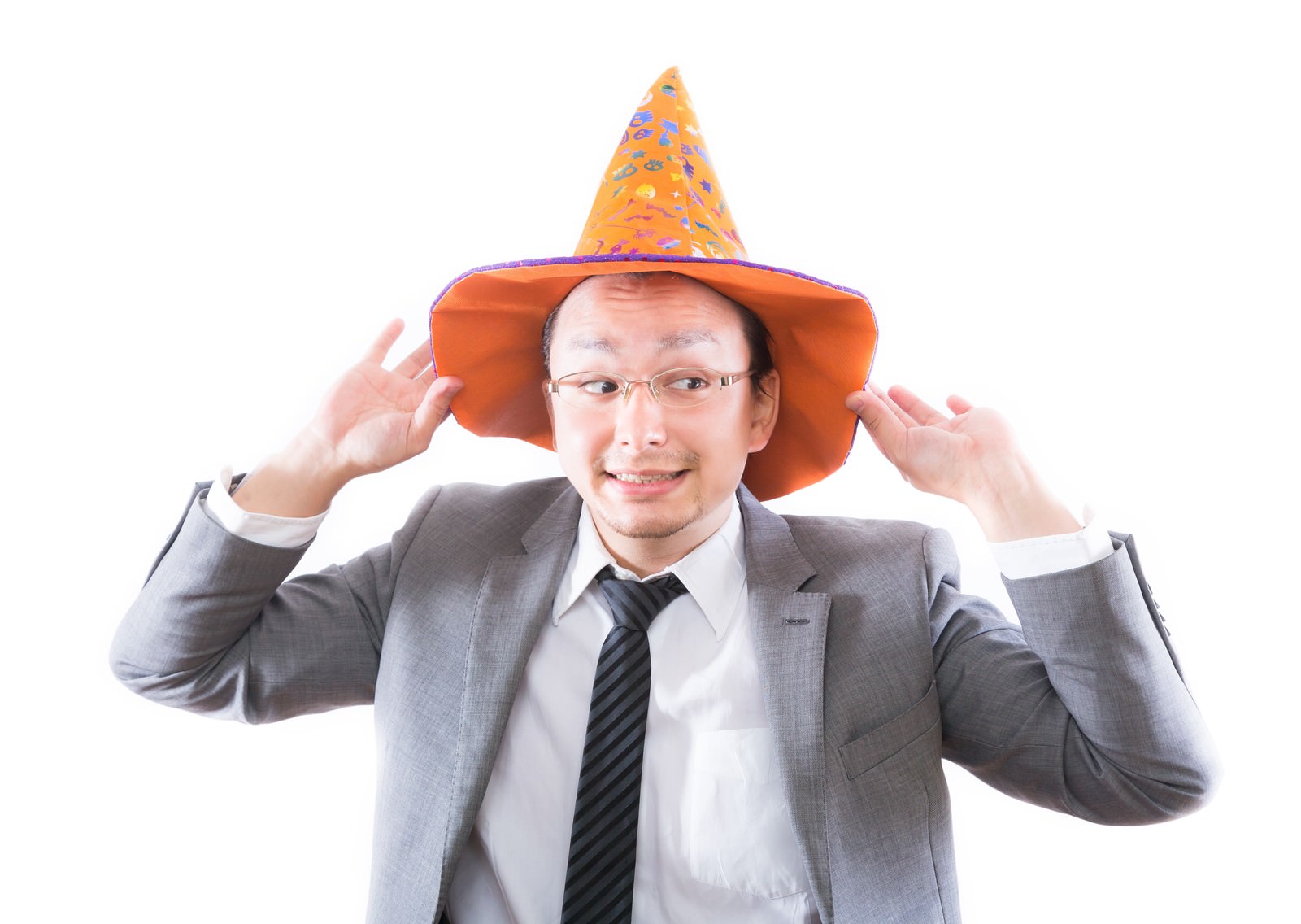 魔女帽子を頭に乗せる薄笑いのスーツ男性［モデル：Max_Ezaki］
