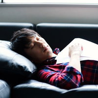 革のソファーで紙を持ったまま寝落ちする男性の写真