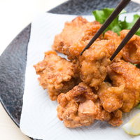 箸でつまんだ唐揚げとレモンが添えられた黒い模様の皿の写真