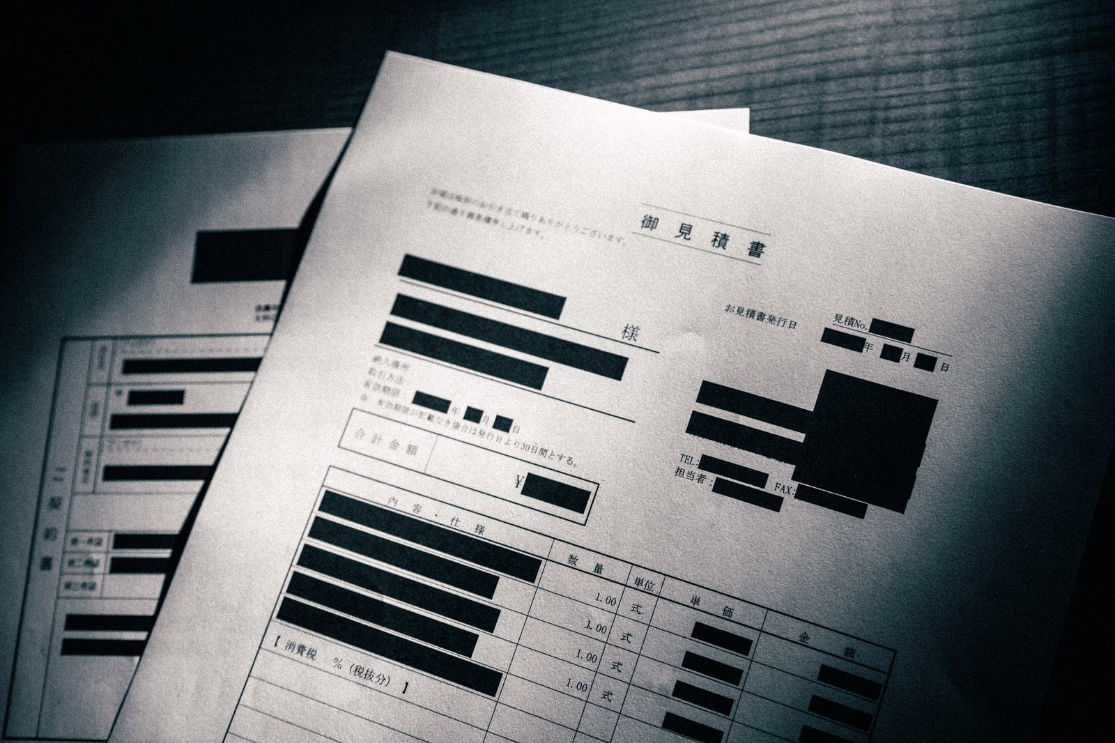 机の上に重ねられた黒塗りされたお見積書の複数枚