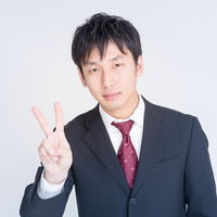 白背景で右手ピースサインをするスーツのビジネスマンの写真