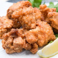 黒い皿にレモンと緑の葉と白い紙を敷いた唐揚げのてんこ盛りの写真