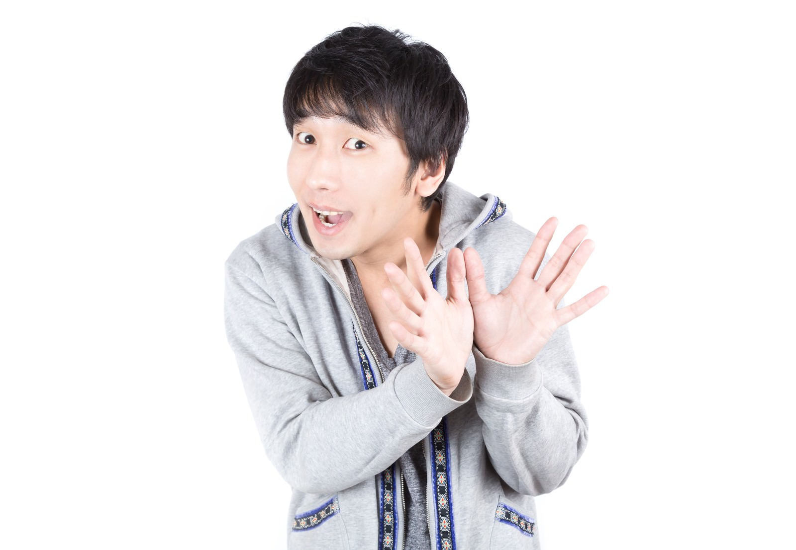 グレーのパーカーの男性が両手を前に出し口を開けて白い背景の前に立っている［モデル：大川竜弥］