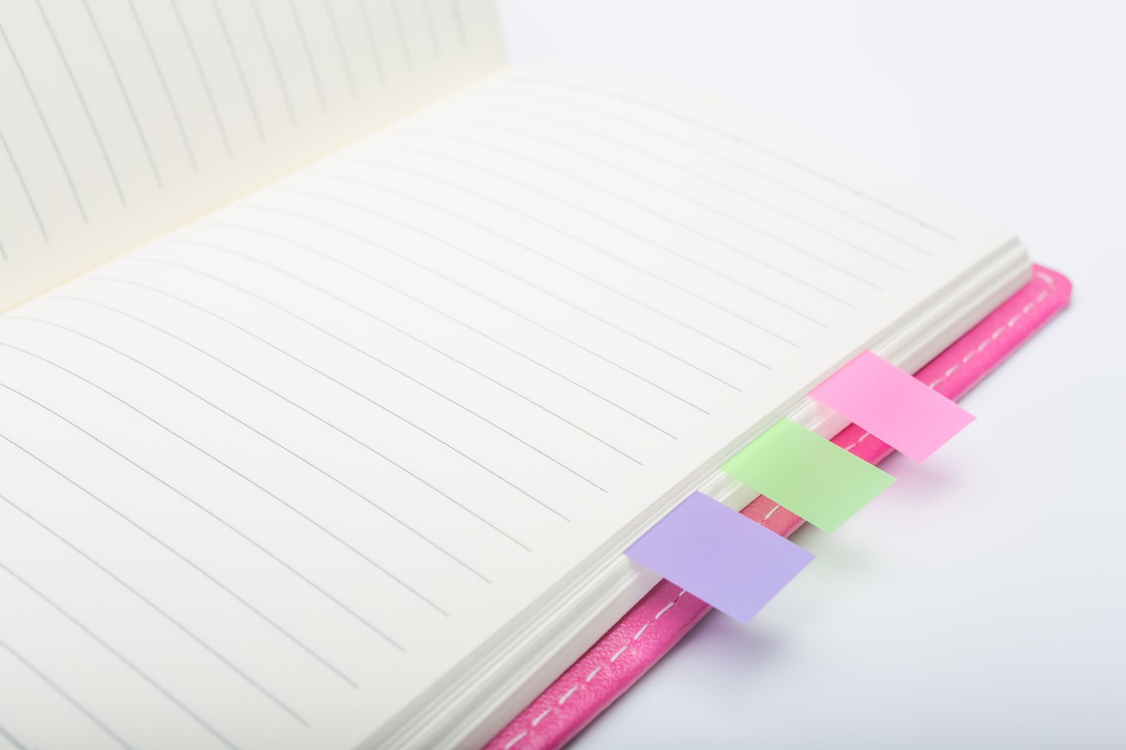 ピンク色の手帳にピンク、緑、紫の付箋を貼った上にペンを置いた写真