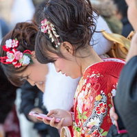 赤い着物でスマートフォンを見る成人式の女性の写真