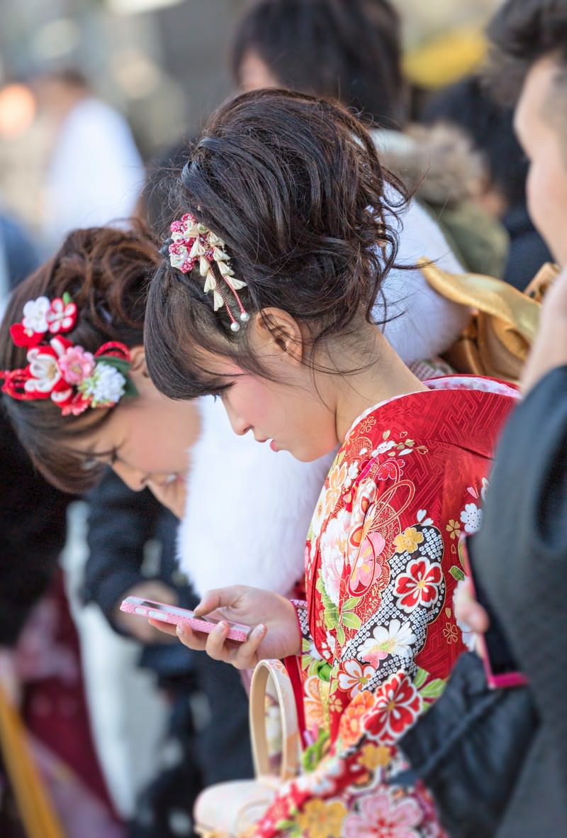 成人式の赤い振袖姿でスマートフォンを持つ女性と、髪飾りの花