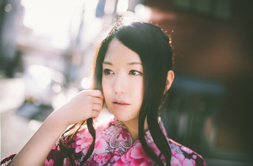 花柄浴衣で髪に手を添えるぼけた街並み背景の女性