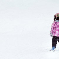 ピンクのチェック柄ジャケットで雪の上に立つスキーの子供の写真
