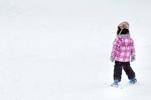 ピンクのチェック柄ジャケットで雪の上に立つスキーの子供