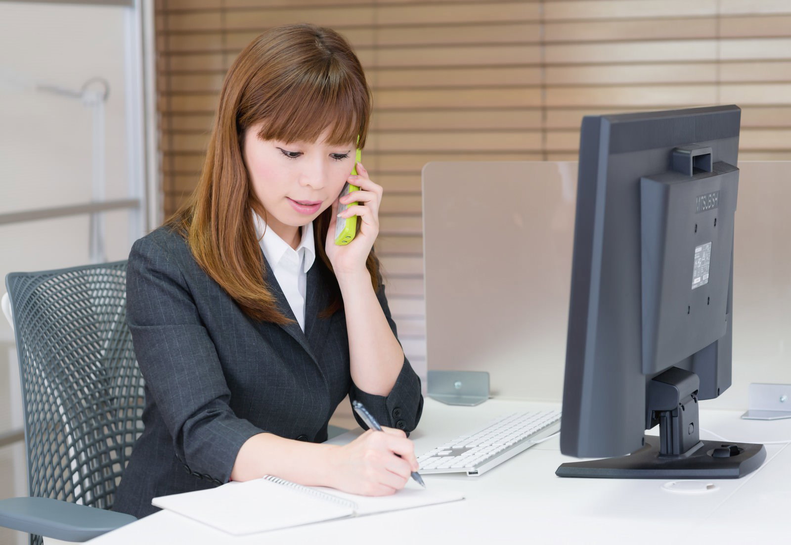 スマートフォンで通話しながらメモを取る女性［モデル：暢子］