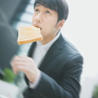 トーストを咥えて下から見上げた角度のスーツ姿のビジネスパーソンの写真