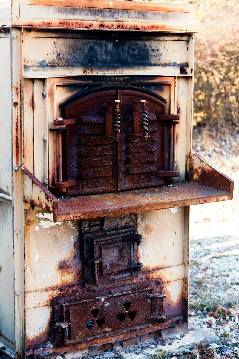 サビが目立つ古い焼却炉。クリーム色の枠に焦げた跡があり、鋳鉄製の投入口と燃焼室が見える