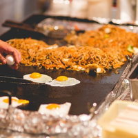 大きな鉄板で目玉焼きと麺を焼く屋台の焼きそば調理の写真