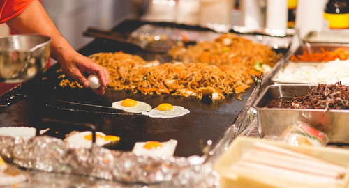 大きな鉄板で目玉焼きと麺を焼く屋台の焼きそば調理