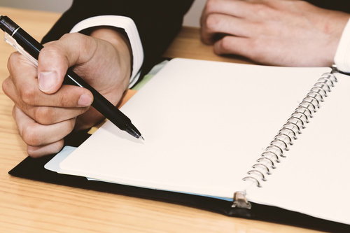 木目の机でノートにペンを走らせる手元