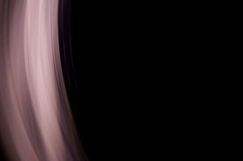 黒い背景の右側に薄いピンクのカーテンが縦に流れる抽象写真
