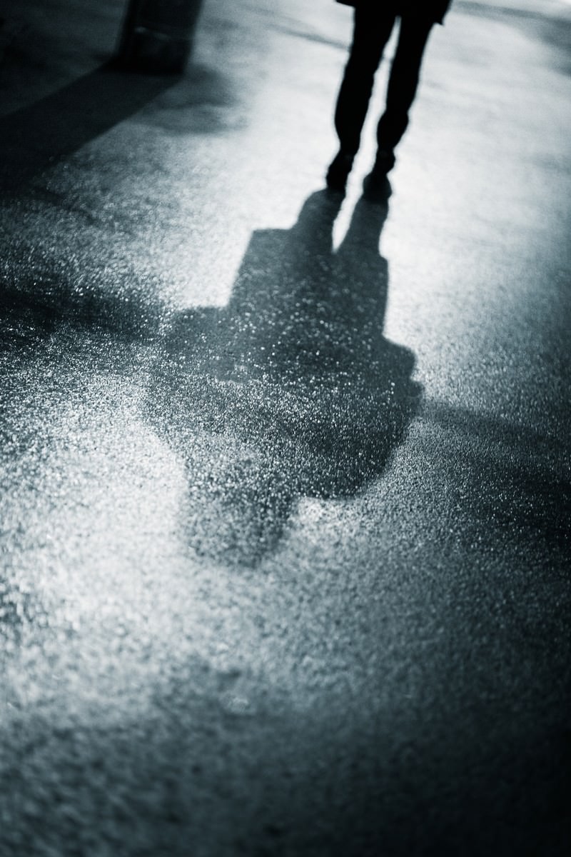雨上がりの夜道を歩く人物の影